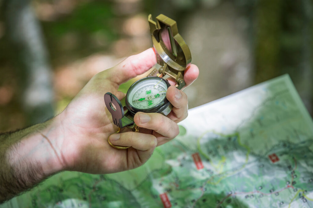 Hiker holding a compass in the woods overtop of a map