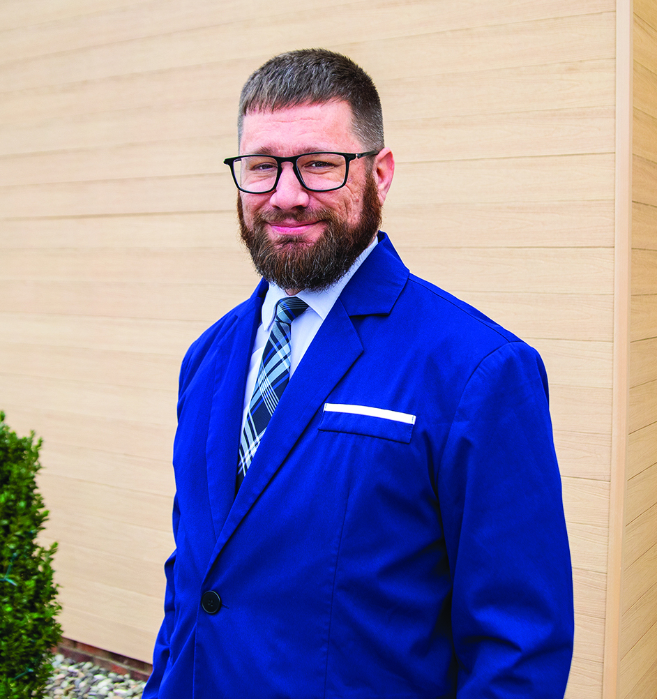 Zach Eddinger, CRPC, Financial Advisor standing in front of a tan wooden background with some small foliage nearby