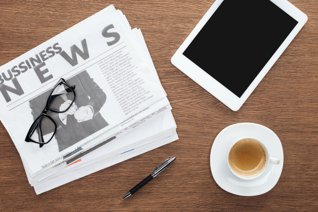 elevated view of cup of coffee, pen, tablet with blank screen and business newspapers on wooden