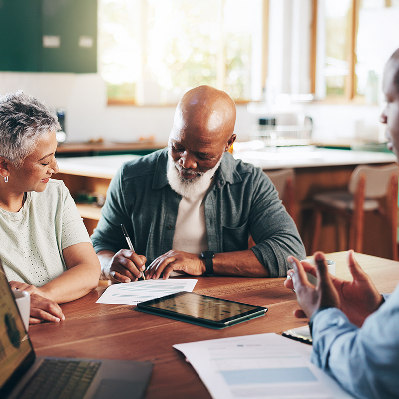 Elderly couple smiling signing a form while talking to an advisor